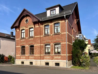 Das denkmalgeschützte Klinkergebäude von der Straßenseite, mit Giebel, Dachgauben und Balkonen.