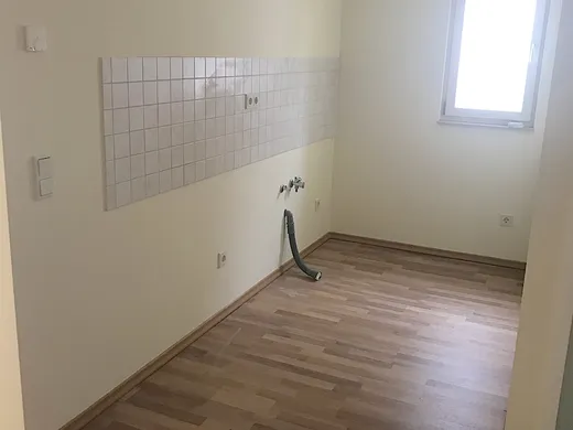 Küchenbereich mit gefliestem Wandstreifen, vorbereiteten Anschlüssen und einem Fenster an der Stirnseite.